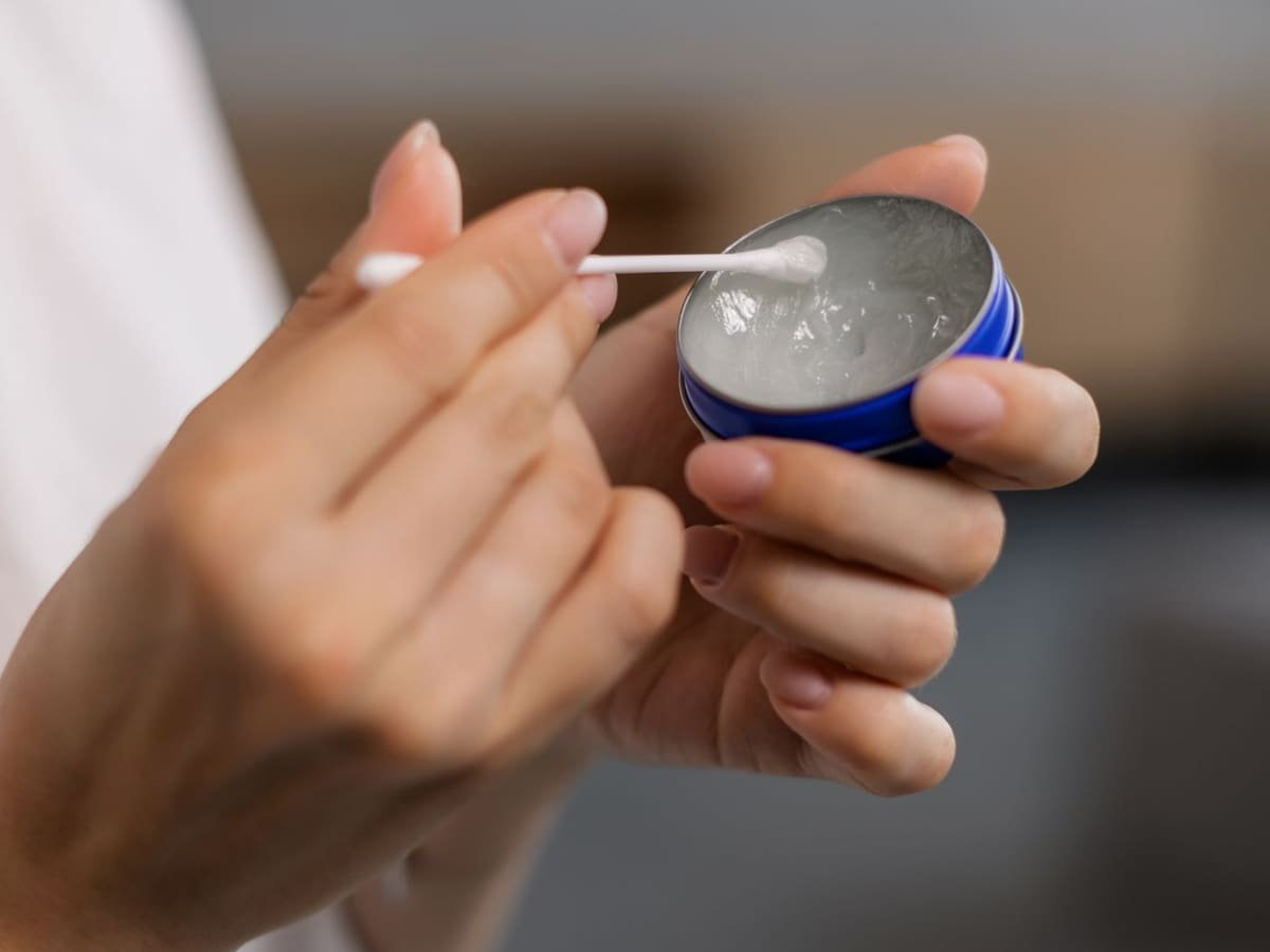 Close-up of a hand applying balm from a small container with a cotton swab