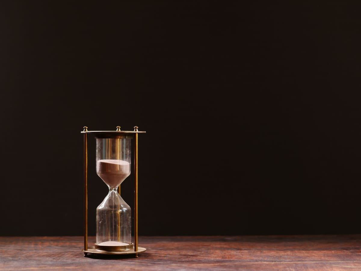 An hourglass with sand trickling through, against a dark background