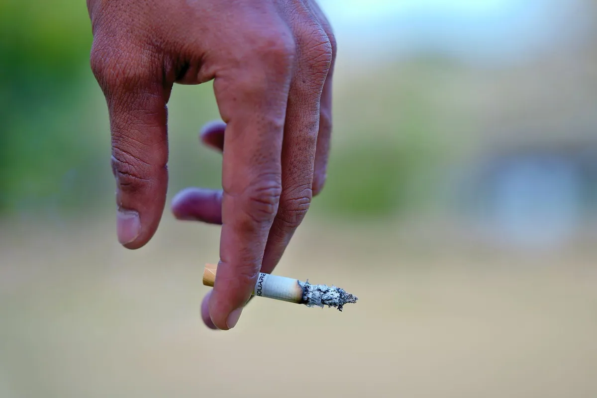 Close-up of a hand holding a burning cigarette, illustrating lung support for smokers and ex-smokers