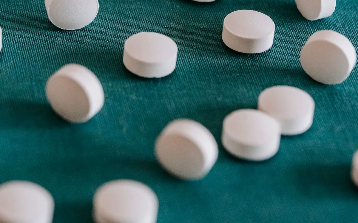 White supplement tablets scattered on a teal surface, illustrating NAC dosage for lung health